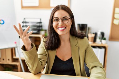 Genç, güzel, İspanyol bir iş kadını masada oturmuş ofiste konuşuyor.