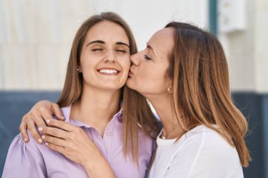 Two women mother and daughter hugging each other and kissing at street