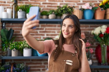 Çiçekçide kendine güvenen güzel İspanyol kadın çiçekçi akıllı telefondan selfie çekiyor.