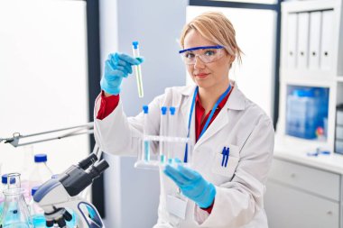 Laboratuvarda test tüpleri tutan genç sarışın bilim kadını.