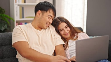 Man and woman couple sitting on sofa using laptop at home