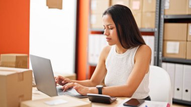 Young beautiful hispanic woman ecommerce business worker using laptop working at office