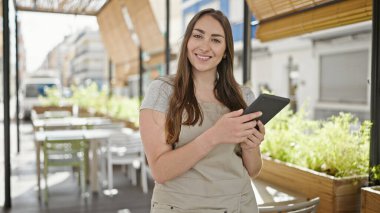 Kahve dükkanının terasında dokunmatik ped kullanarak gülümseyen genç ve güzel İspanyol bayan garson.