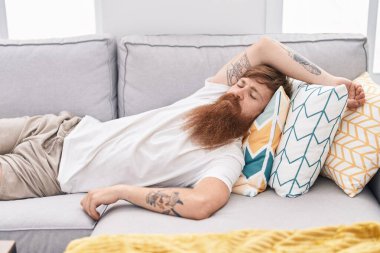 Genç kızıl saçlı adam kanepede uzanıyor ve evde uyuyor.