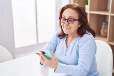 Evde masada oturan son sınıf öğrencisi akıllı telefon kullanıyor.