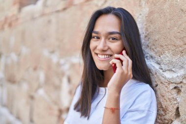 Genç, güzel, İspanyol bir kadın gülümsüyor ve caddede akıllı telefondan konuşuyor.