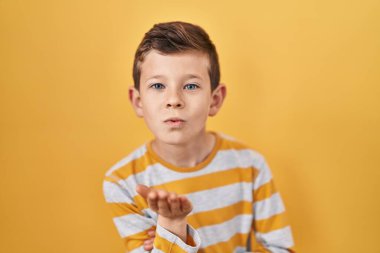 Beyaz tenli genç, sarı arka planda durup kameraya bakarak havayla öpüşüyor ve güzel ve seksi oluyor. aşk ifadesi. 