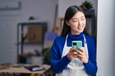 Chinese woman artist smiling confident using smartphone at art studio