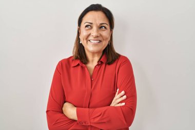Latin kökenli olgun bir kadın beyaz arka planda durup gülümsüyor, yan tarafa bakıyor ve düşünüyor.. 