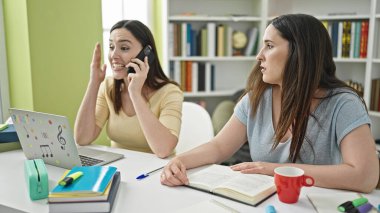 Kütüphane üniversitesinde akıllı telefon sohbeti için rahatsız edici iki kadın.