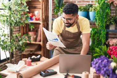 Young arab man florist using laptop reading document at florist