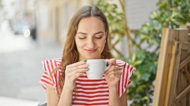 Kahve dükkanının terasında bir fincan kahve içen genç sarışın kadın.