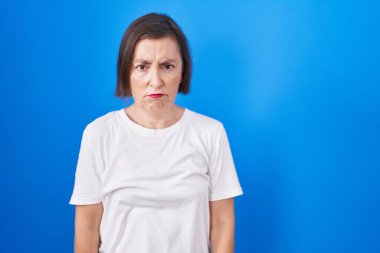 Middle age hispanic woman standing over blue background depressed and worry for distress, crying angry and afraid. sad expression. 
