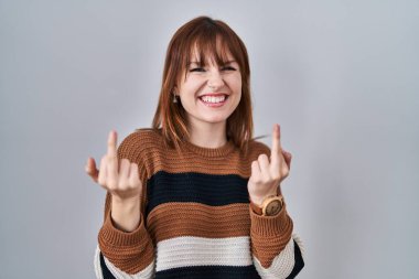 Young beautiful woman wearing striped sweater over isolated background showing middle finger doing fuck you bad expression, provocation and rude attitude. screaming excited 