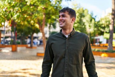 Genç İspanyol adam gülümsüyor parkın kenarına bakıyor.