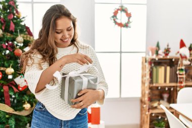 Genç, güzel, İspanyol bir kadın gülümseyerek evinde kendine güvenen bir Noel hediyesi açıyor.