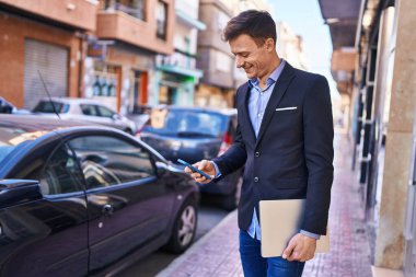 Young man business worker using smartphone holding laptop at street