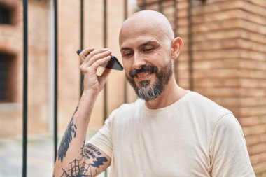 Young bald man smiling confident listening audio message by the smartphone at street