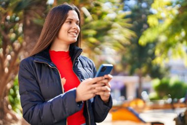 Parkta akıllı telefon kullanarak gülümseyen güzel bir İspanyol kadın.