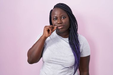 Pembe arka planda duran genç Afrikalı kadın ağzı ve dudakları parmakları fermuar gibi kapalı. gizli ve sessiz, tabu konuşması 