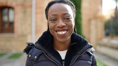 Afro-Amerikalı kadın parkta kendinden emin bir şekilde gülümsüyor.