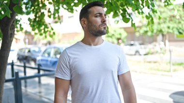 Latin kökenli genç adam ciddi bir ifadeyle sokağa bakıyor.