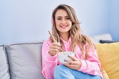 Young woman listening to music eating chinese food at home