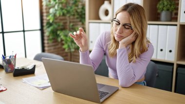 Genç, güzel İspanyol iş kadını ofiste sıkıcı bir ifadeyle dizüstü bilgisayar kullanıyor.