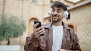 Genç Arap adam kendinden emin bir şekilde gülerek sokakta müzik dinliyor.