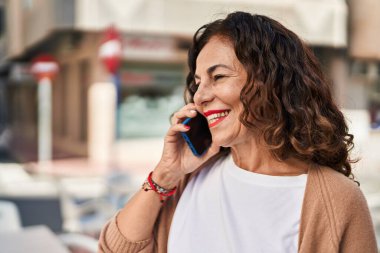 Middle age hispanic woman speaking on the phone outdoors