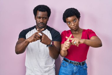 Genç Afrikalı Amerikalı çift pembe arka planda duruyor. Reddedilme ifadesi negatif işaret veriyor. 