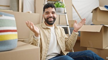 Young hispanic man smiling confident sitting on floor at new home
