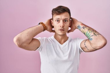 Pembe arka planda duran beyaz adam deli ve elleri başının üstünde korkmuş, korkmuş ve ağzı açık şoktan şaşırmış. 