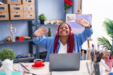 African american woman artist listening to music sitting on table at art studio