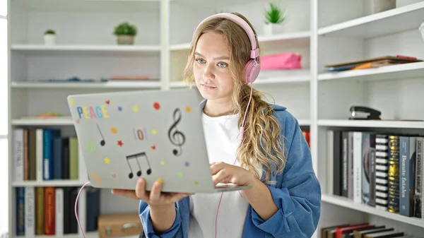 Kütüphanede dizüstü bilgisayar ve kulaklık kullanan genç sarışın kız öğrenci.