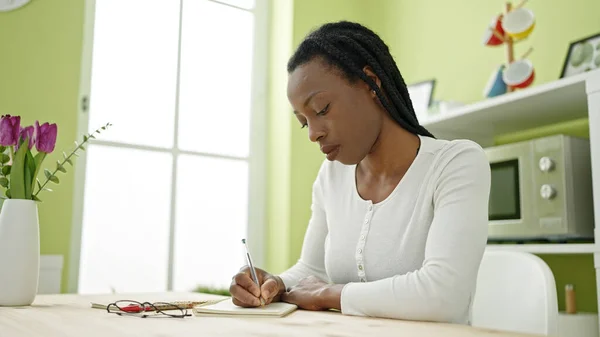 アフリカ系アメリカ人の女性がノートを書いて家のテーブルの上に座って — ストック写真