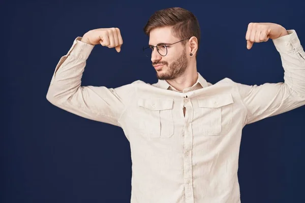 一个留着胡子的西班牙男人站在蓝色的背景上 露出胳膊肌肉 露出自豪的笑容 健身概念 — 图库照片