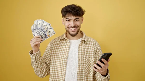 Молодий Арабський Чоловік Використовує Смартфон Тримає Долари Над Ізольованим Жовтим — стокове фото