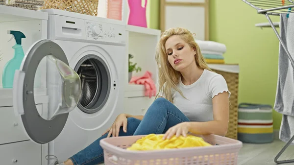 洗濯室で考えている床に座っている若い金髪の女性 — ストック写真