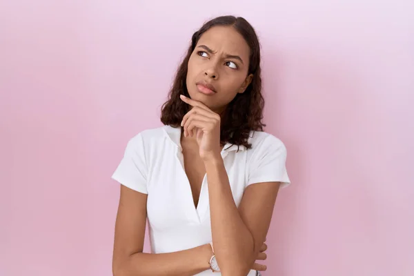 カジュアルな白いTシャツを着た若いヒスパニック系の女性は 質問を心配し 顎に手で心配し 緊張しています — ストック写真