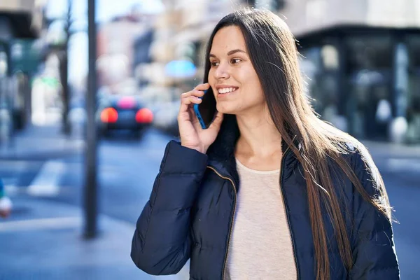 Genç, güzel, İspanyol bir kadın gülümsüyor ve caddede akıllı telefondan konuşuyor.
