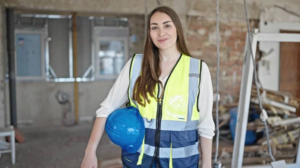 年轻美丽的惊慌失措的女建筑工人带着自信的笑容在建筑工地拿着硬礼帽 — 图库照片