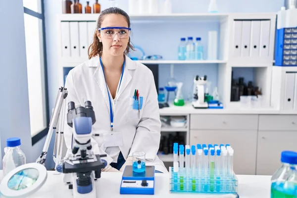 Young hispanic woman working at scientist laboratory relaxed with serious expression on face. simple and natural looking at the camera. 