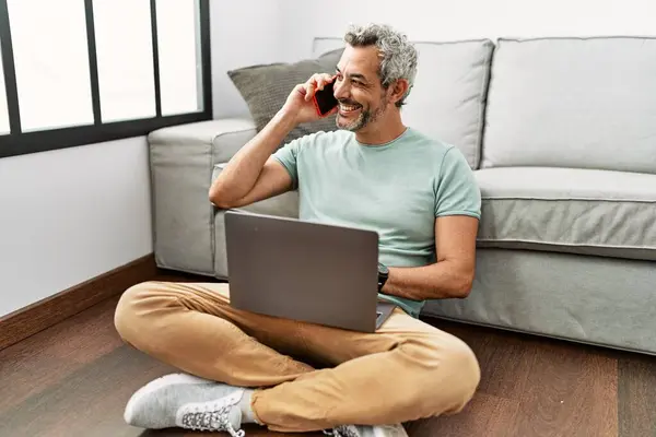 Medelålders Gråhårig Man Talar Smartphone Med Bärbar Dator Sitter Golvet — Stockfoto