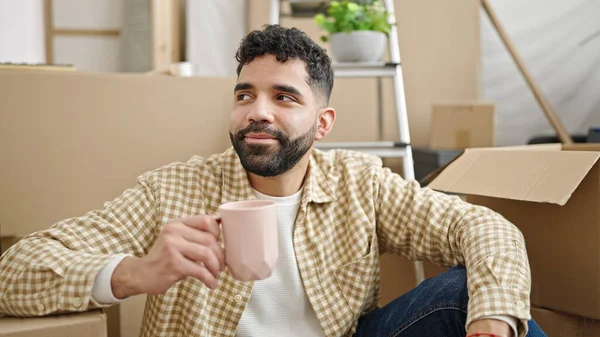 年轻的惊慌失措的男人坐在新家的地板上喝咖啡 — 图库照片