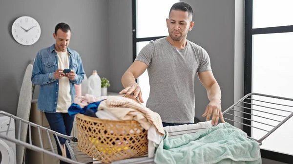 两个男人在洗衣房用智能手机挂衣服 — 图库照片