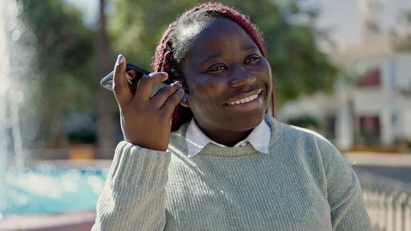 非洲女人在公园用智能手机剪辫子听语音信息 — 图库照片