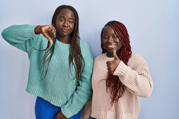 Две Африканки Стоящие Синем Фоне Делающие Большие Пальцы Вверх Вниз — стоковое фото