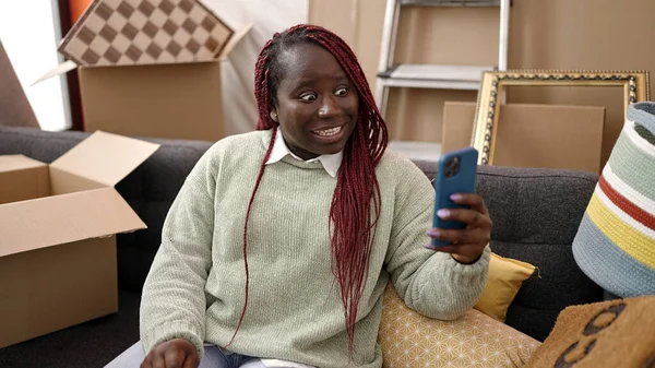 在新家的沙发上 一个留着辫子的非洲女人正在做视频通话 — 图库照片