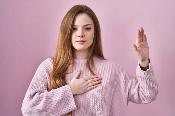 年轻的高加索女人站在粉色的背景之上 双手放在胸前 张开手掌 发誓效忠 — 图库照片